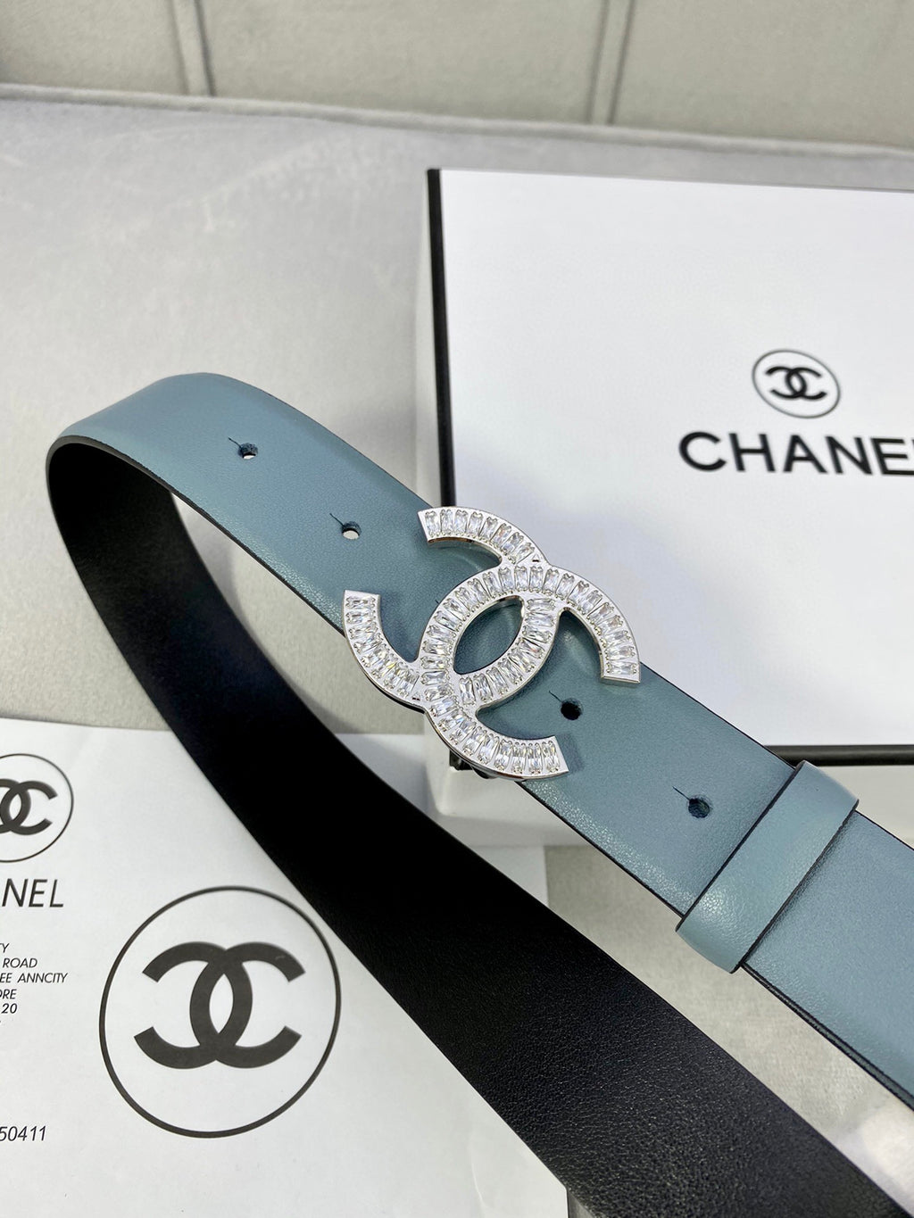 Light blue Chanel belt with silver-toned CC buckle resting beside a Chanel box.