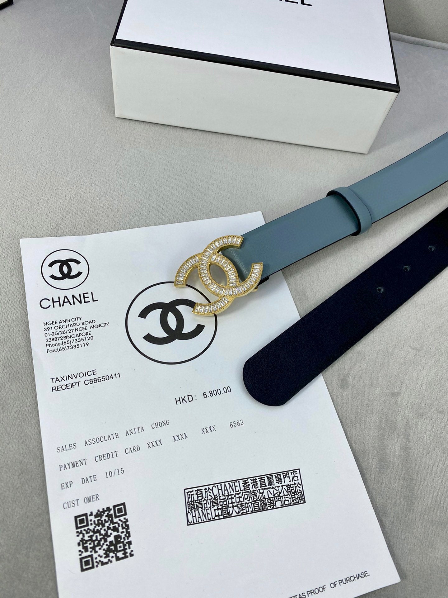 Light blue Chanel belt laid across documents with gold-toned CC buckle.