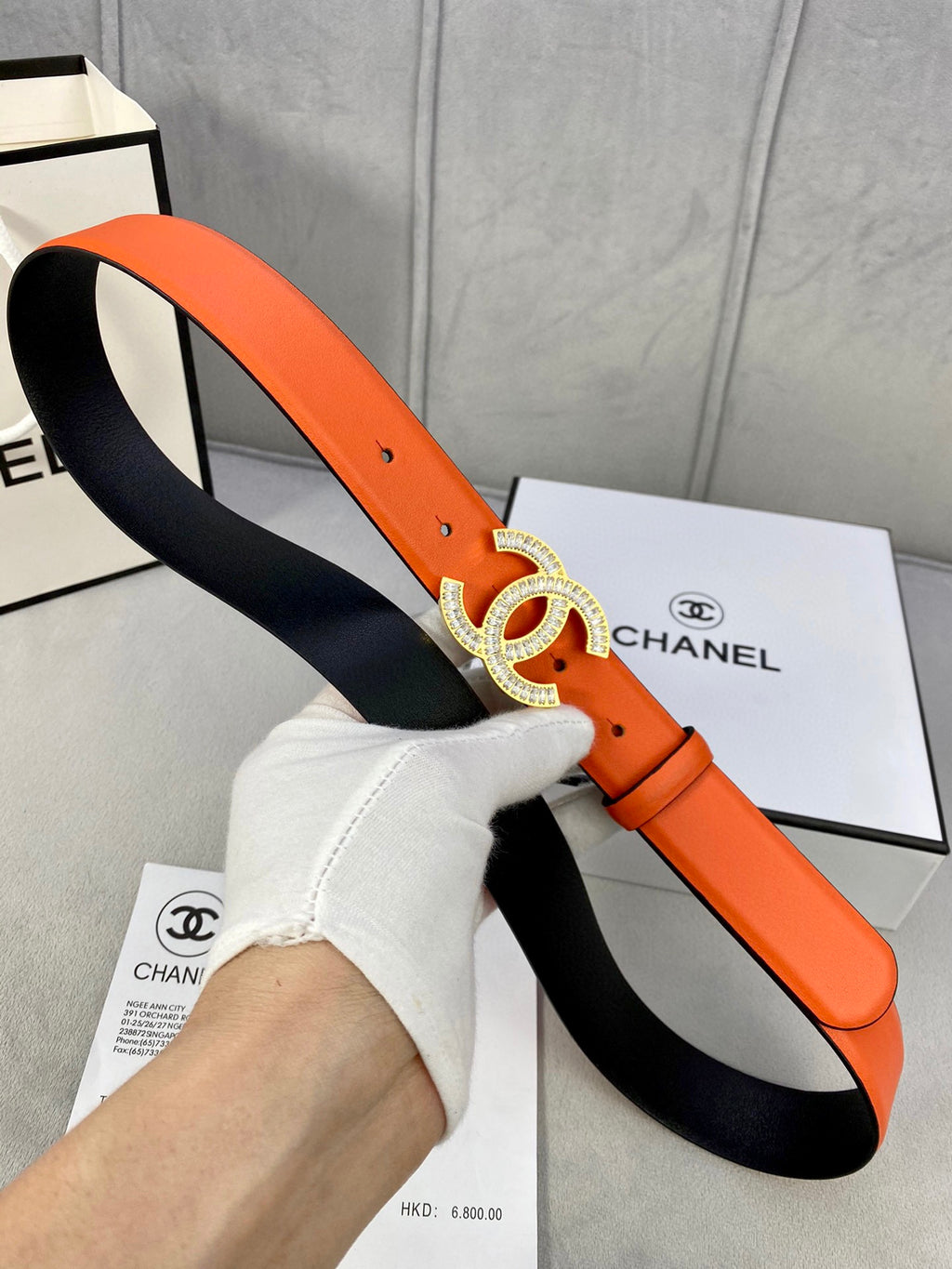 Chanel orange belt with crystal CC buckle and black underside, held by hand