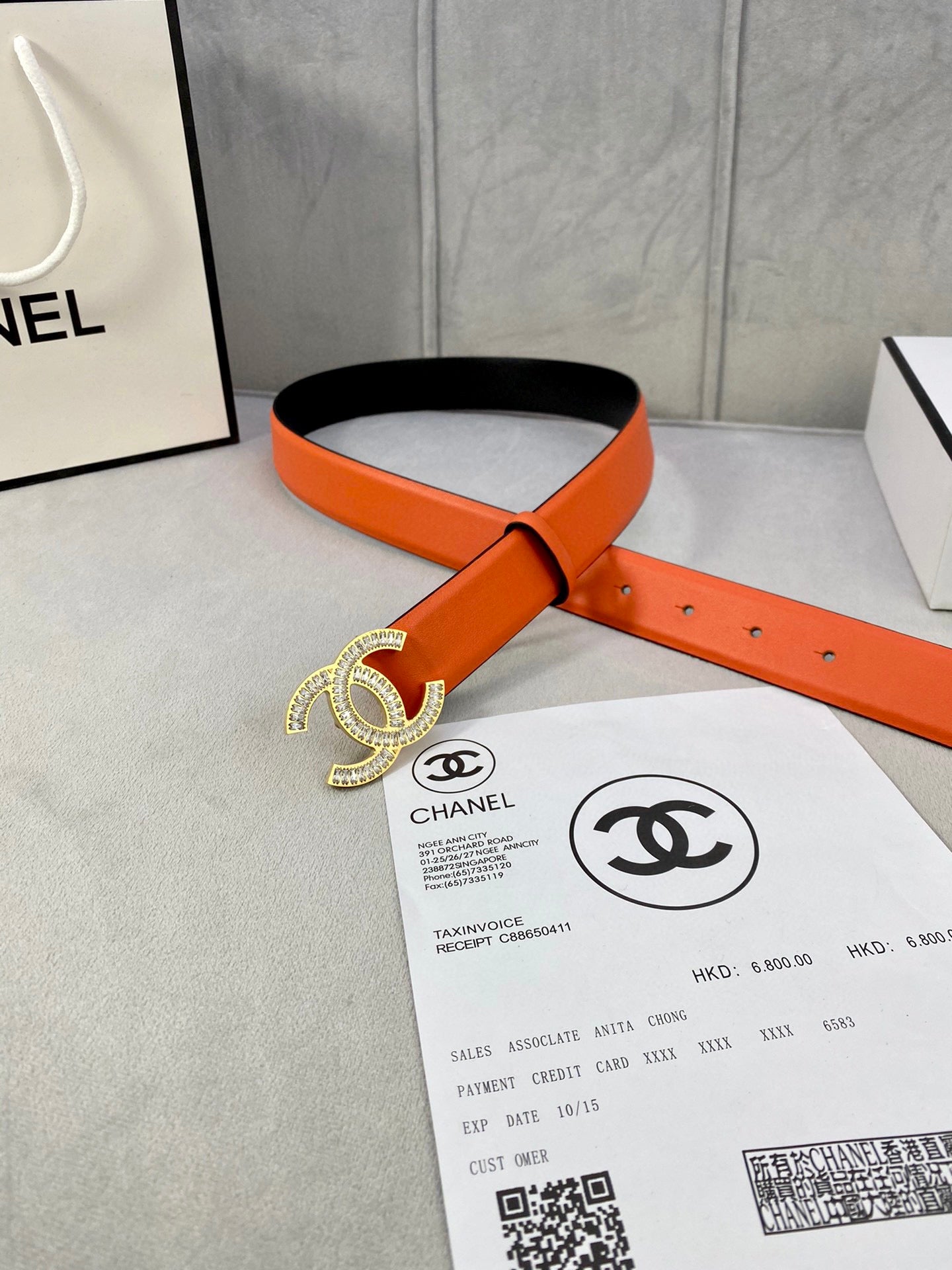 Chanel orange belt with black underside and crystal CC buckle, shown on packaging