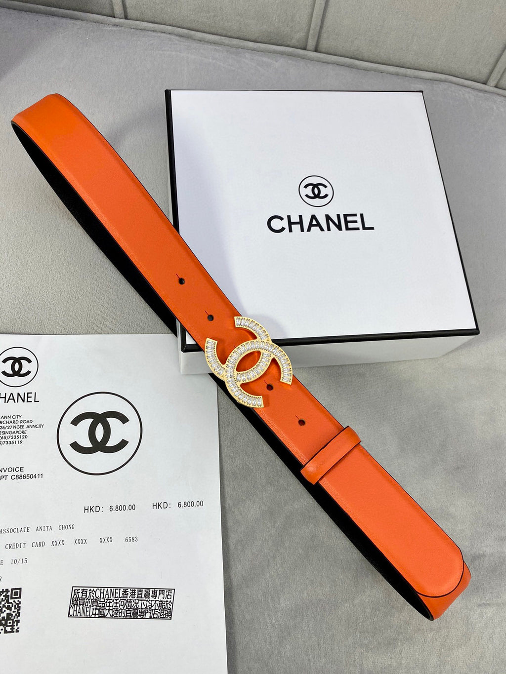 Chanel orange belt with crystal CC buckle on orange strap, laid on box