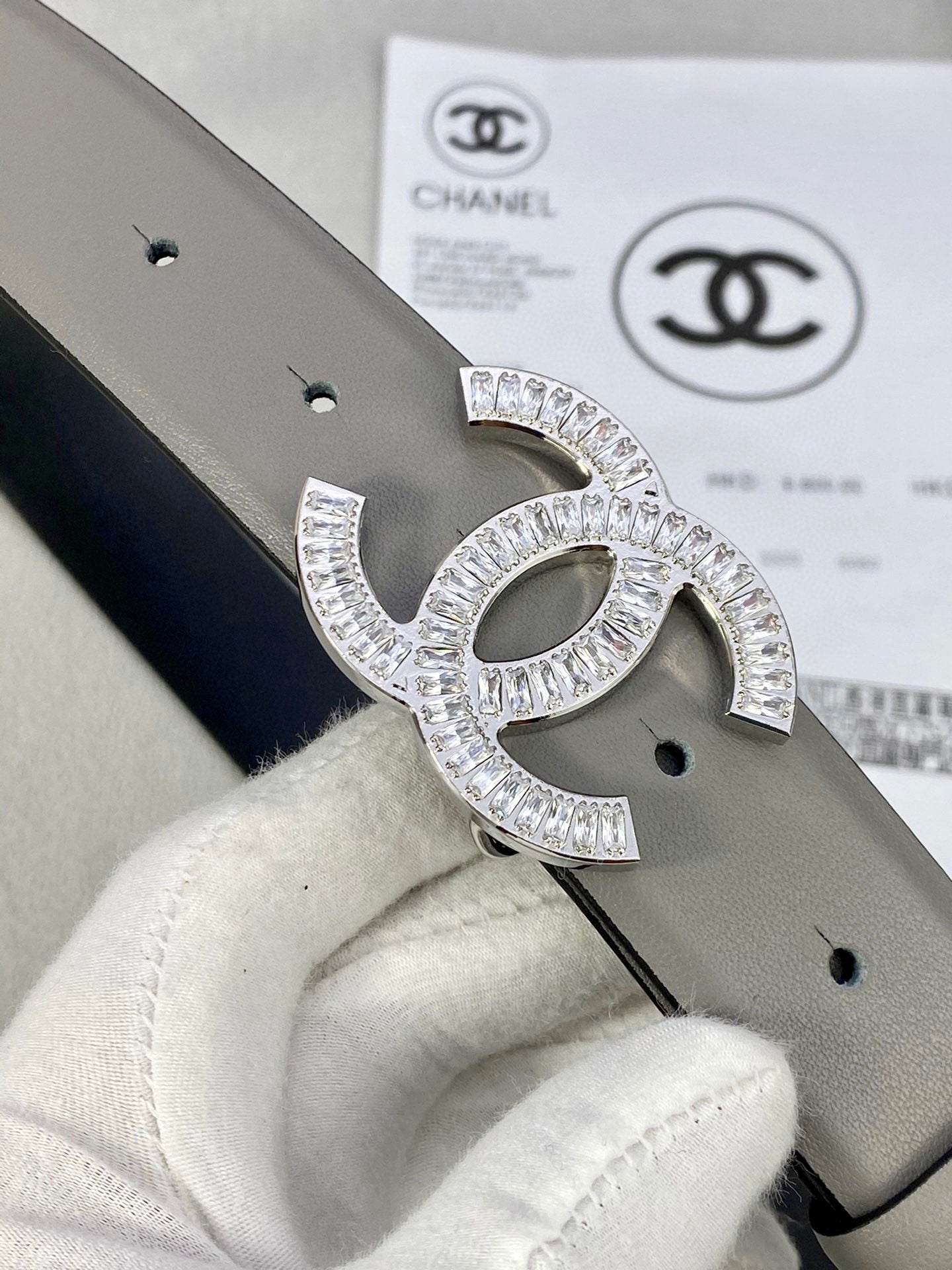 Chanel belt buckle close-up with rhinestone CC design on light gray leather