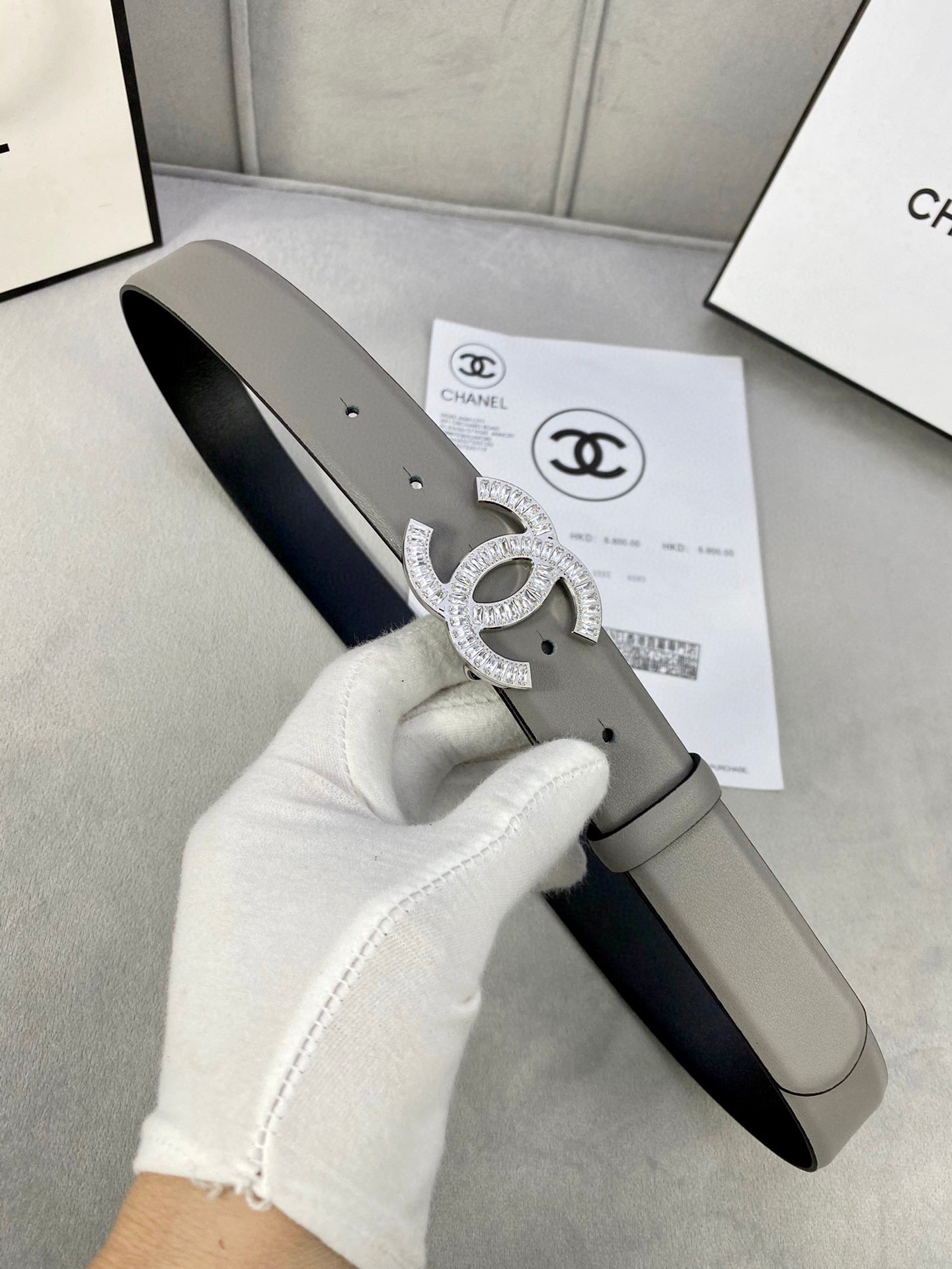 Chanel belt held in hand: light gray leather with gold-tone CC buckle detail