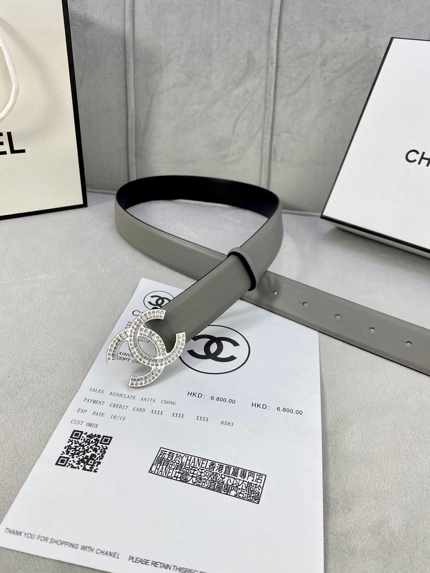 Chanel belt with light gray strap and gold-tone CC buckle, laid on paperwork
