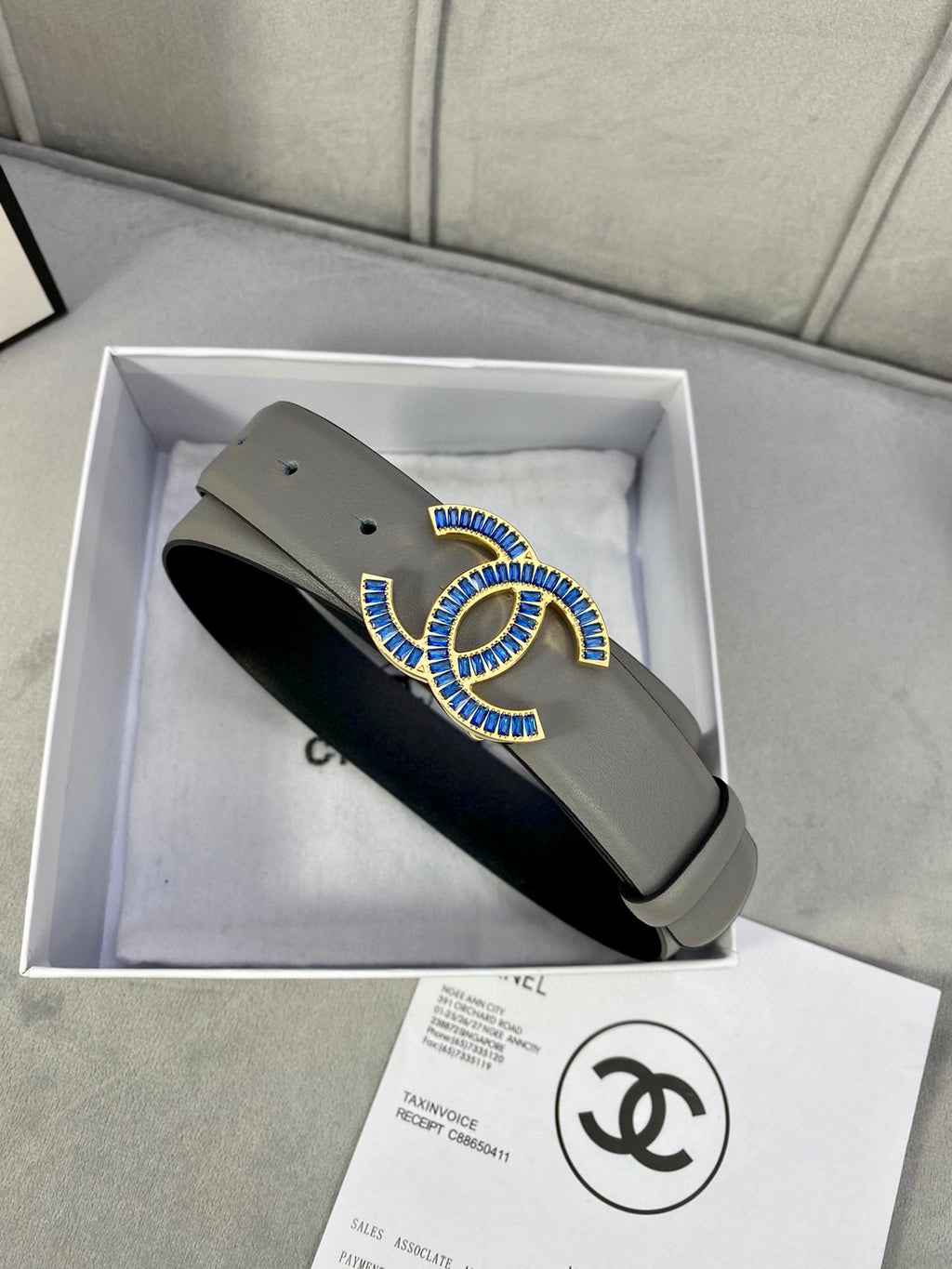 Grey leather belt with blue-and-gold CC buckle, shown from side angle