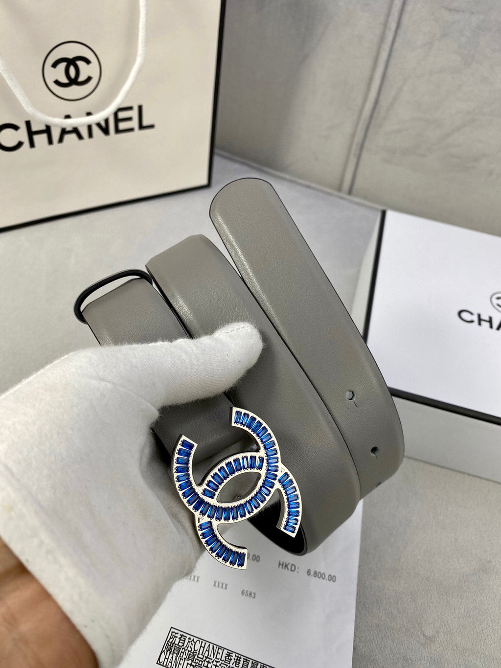 Grey leather belt with blue-and-gold CC buckle, with protective glove