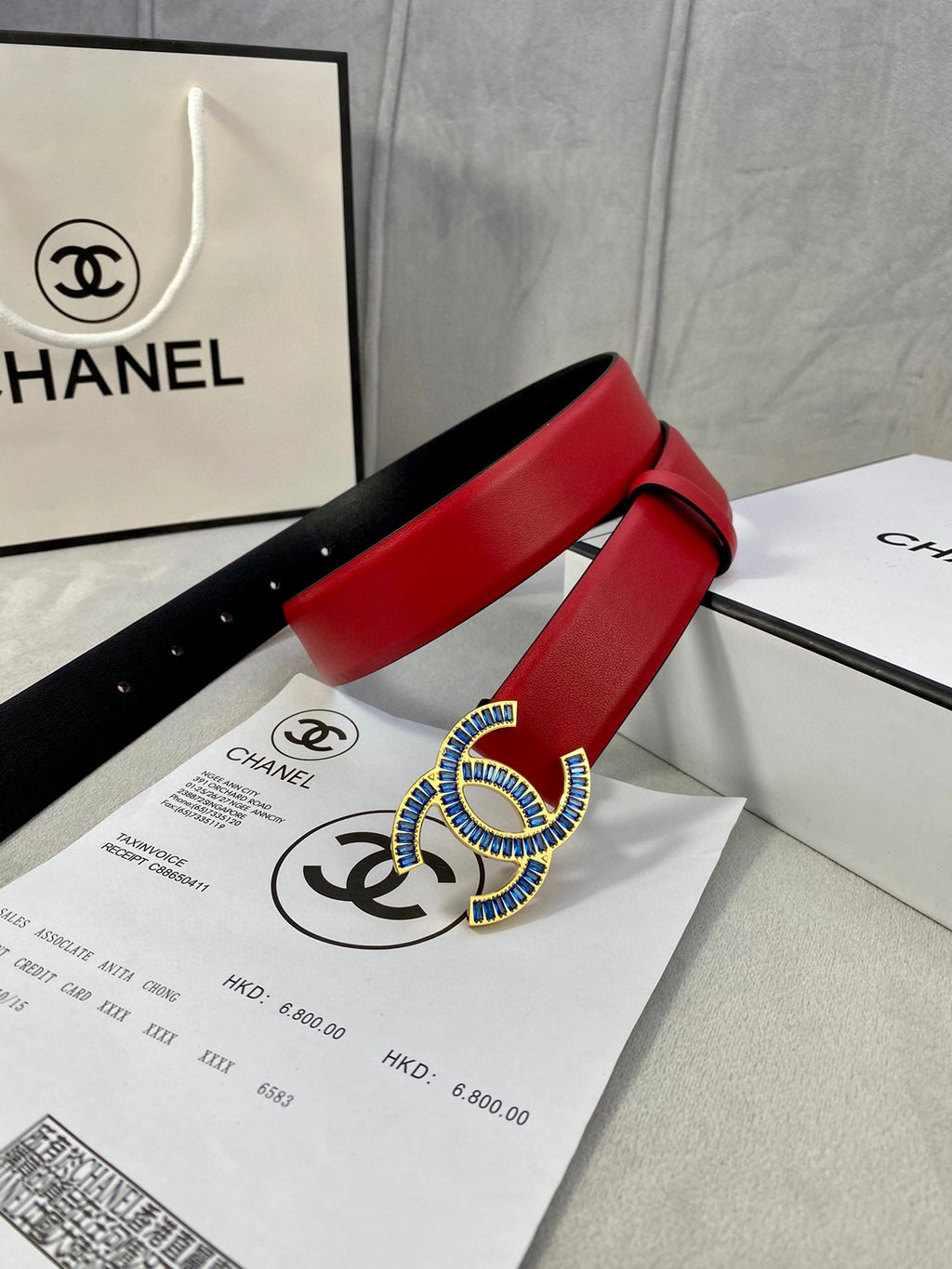 Red leather belt with blue-and-gold CC logo buckle and pin-hole strap on papers