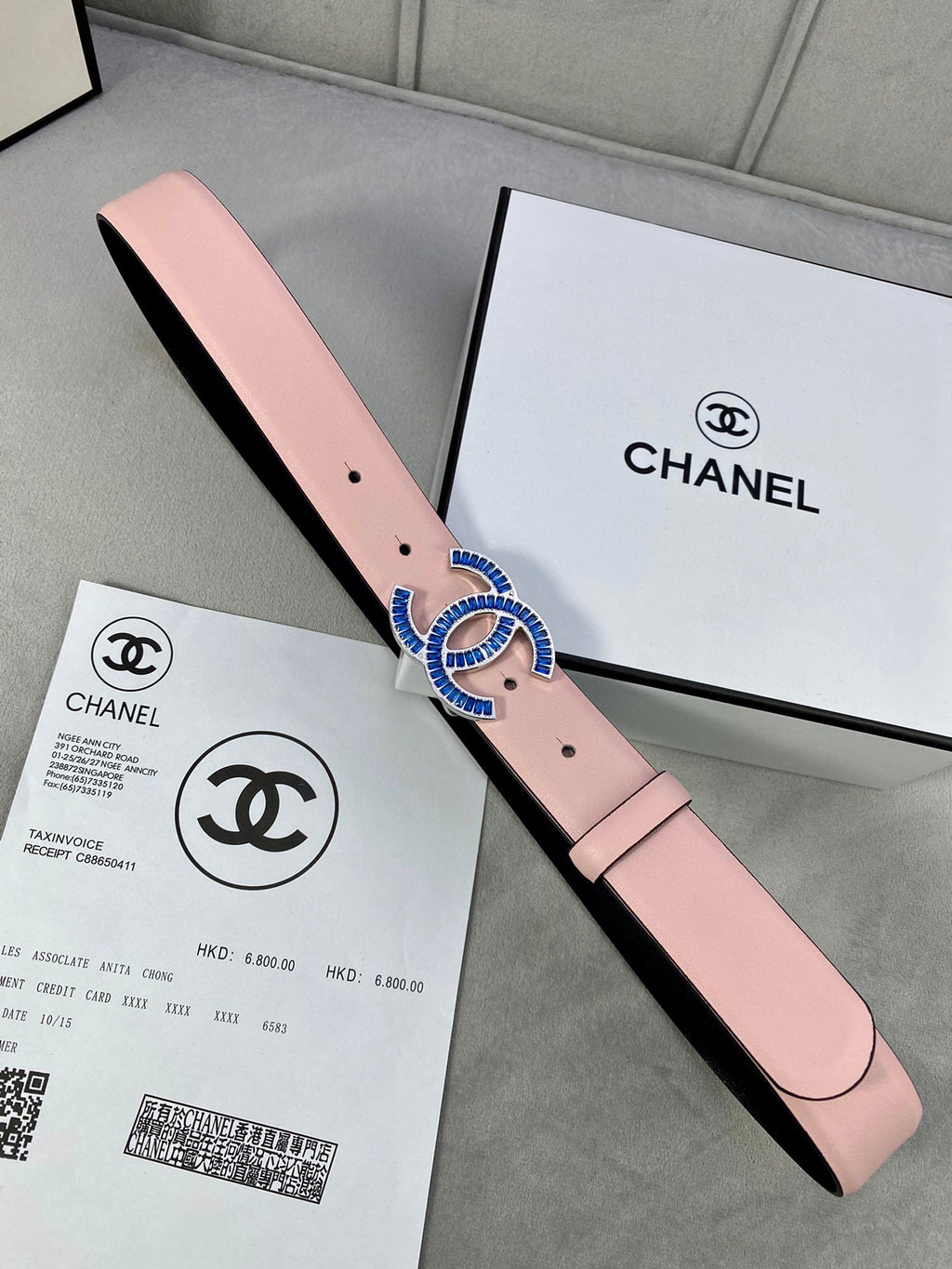 Pink leather belt with blue-and-gold CC buckle on a black-lined strap