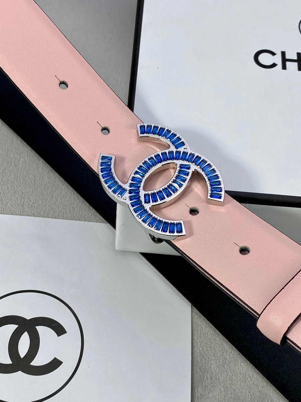 Close-up of pink leather belt with blue-and-gold CC logo buckle and holes