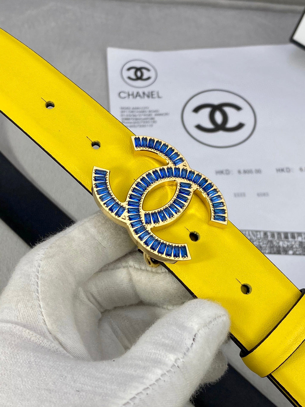 Close-up of yellow Chanel belt with blue CC buckle and metal eyelets