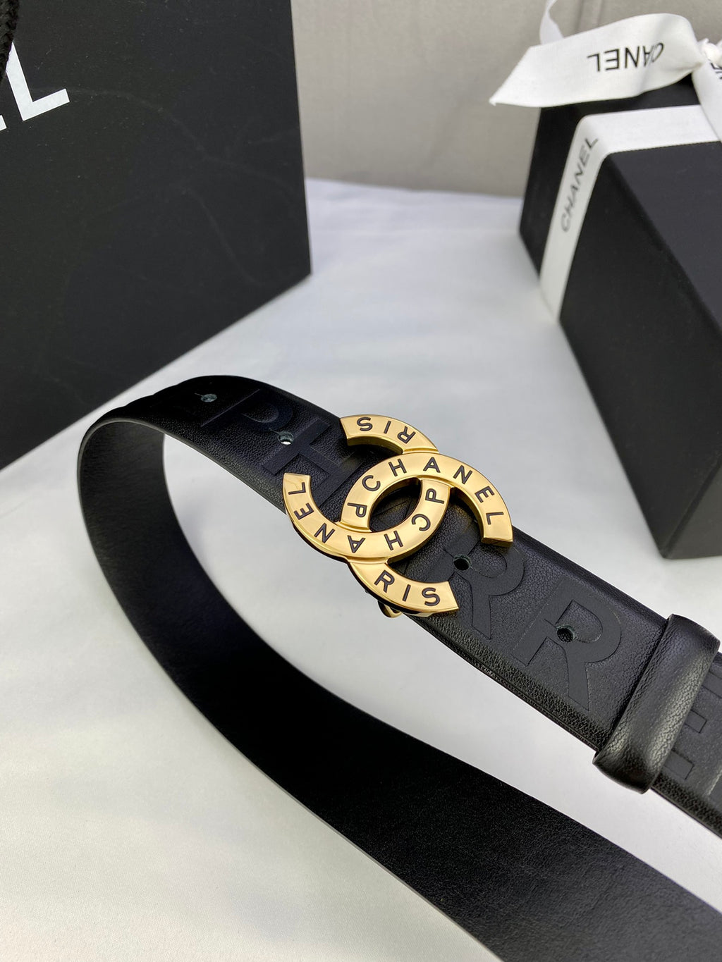 Chanel belt close-up: dark embossed strap with gold-tone circular logo buckle