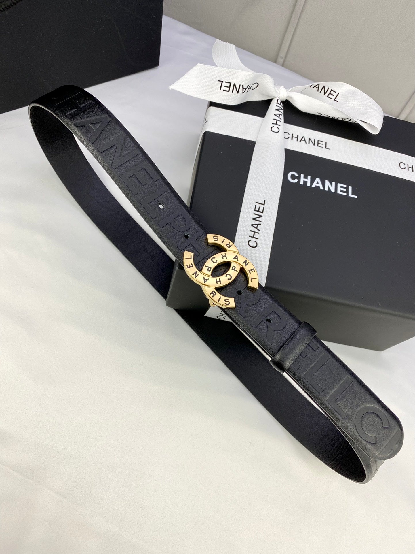 Chanel belt with dark strap, embossed pattern, and gold-tone circular buckle