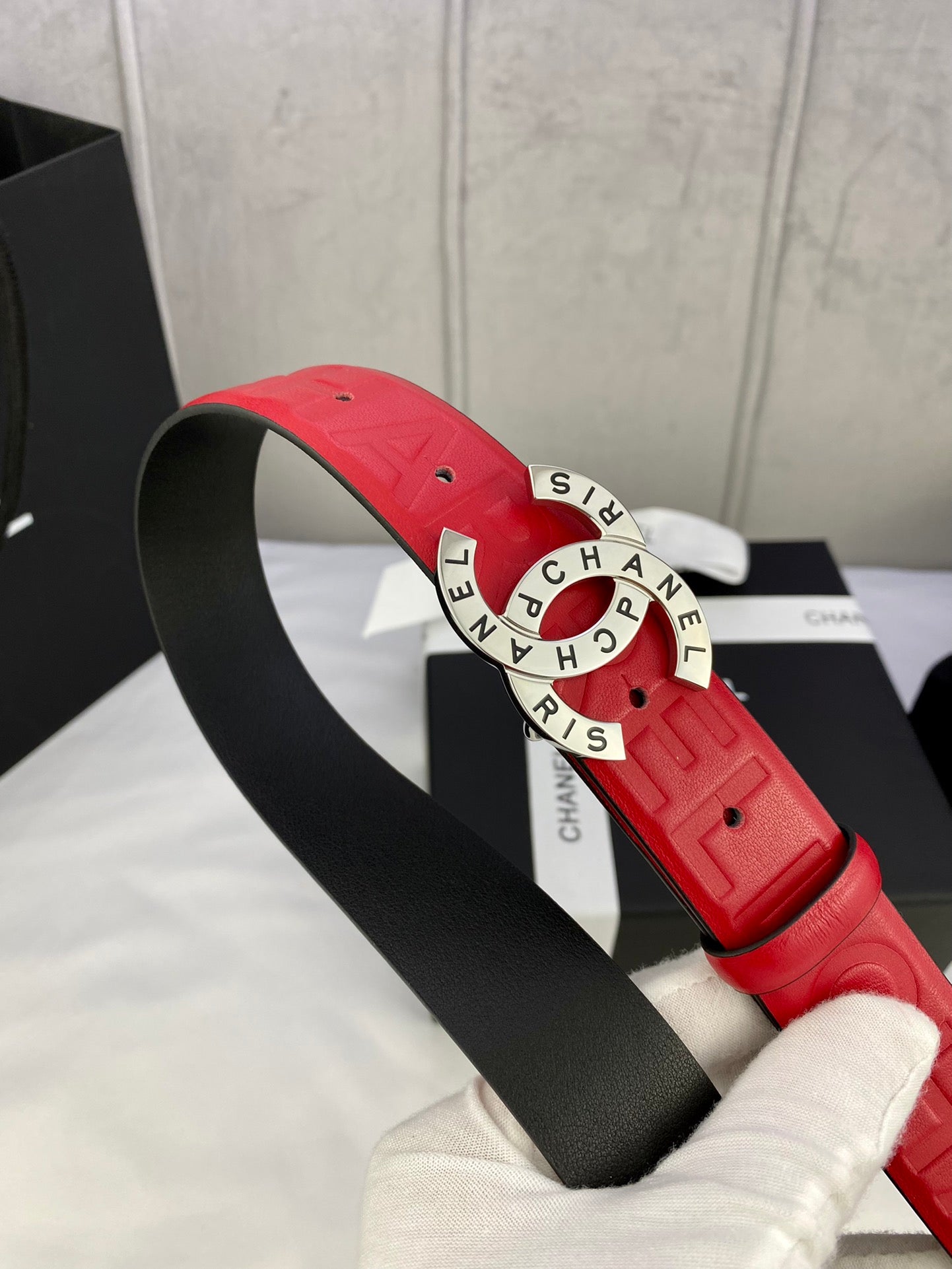 Red Chanel belt with embossed strap and gold circular CHANEL buckle on black strap base