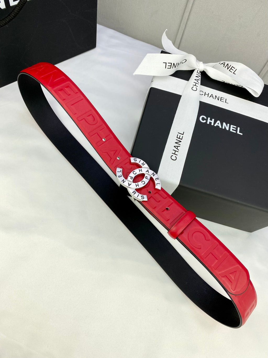 Red Chanel belt with embossed strap and gold circular CHANEL buckle, flat view