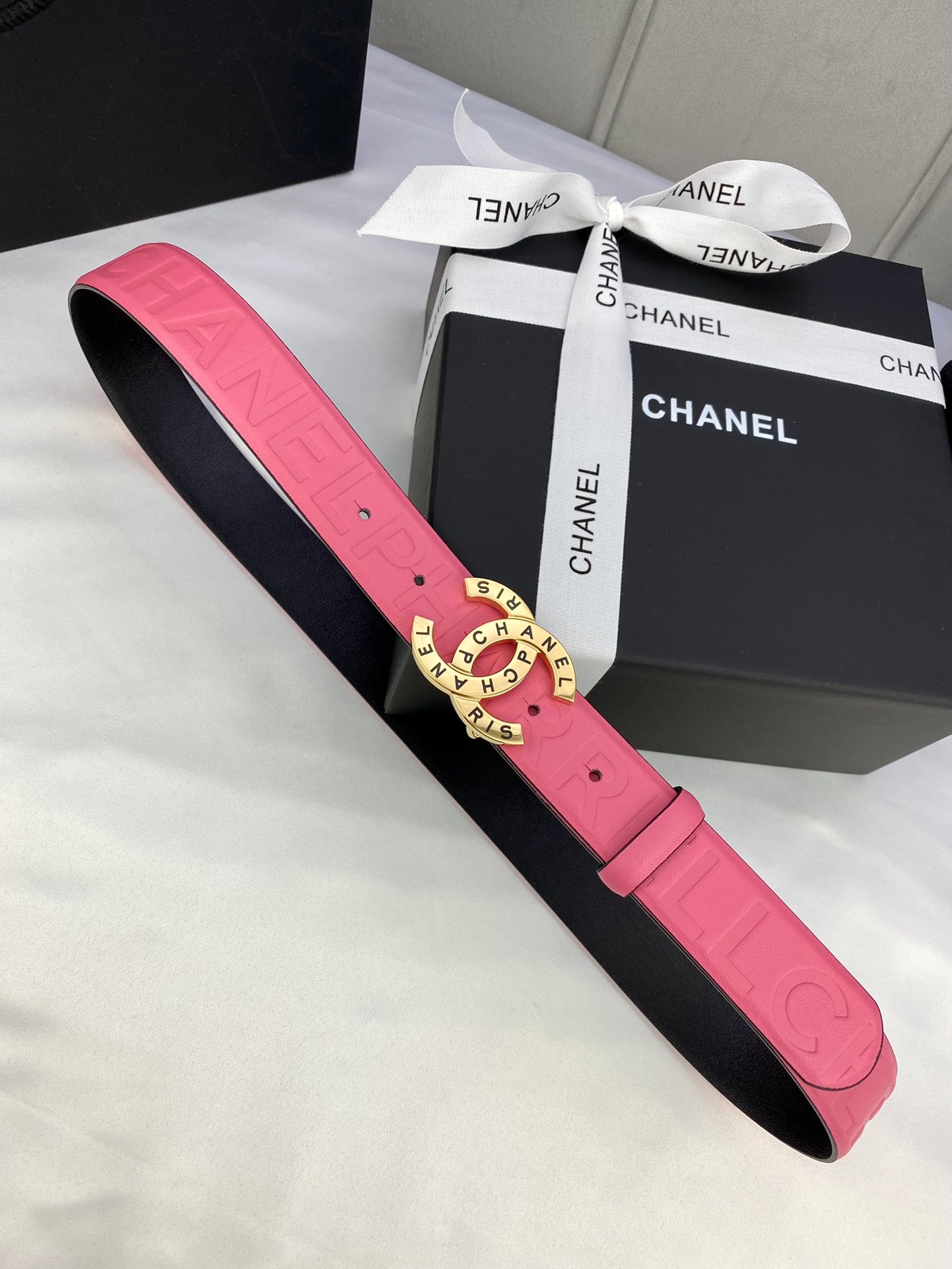Pink Chanel belt with gold circular logo buckle and embossed strap pattern