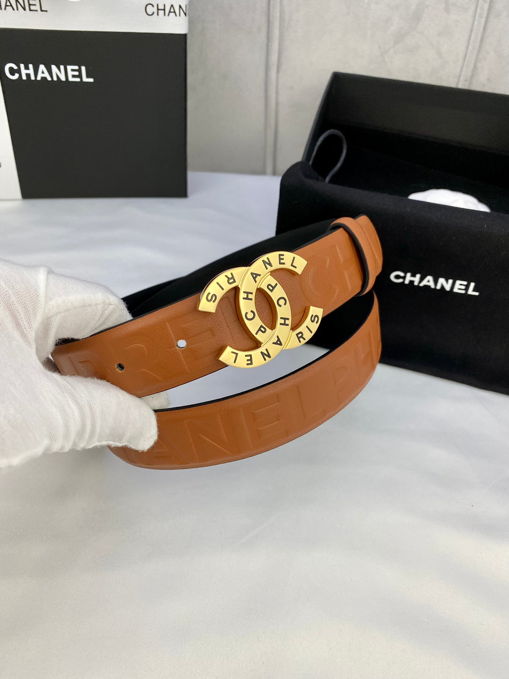 Tan-orange leather belt with circular logo buckle and embossed strap sections.