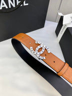 Tan-orange leather belt with circular logo buckle and visible strap edges.