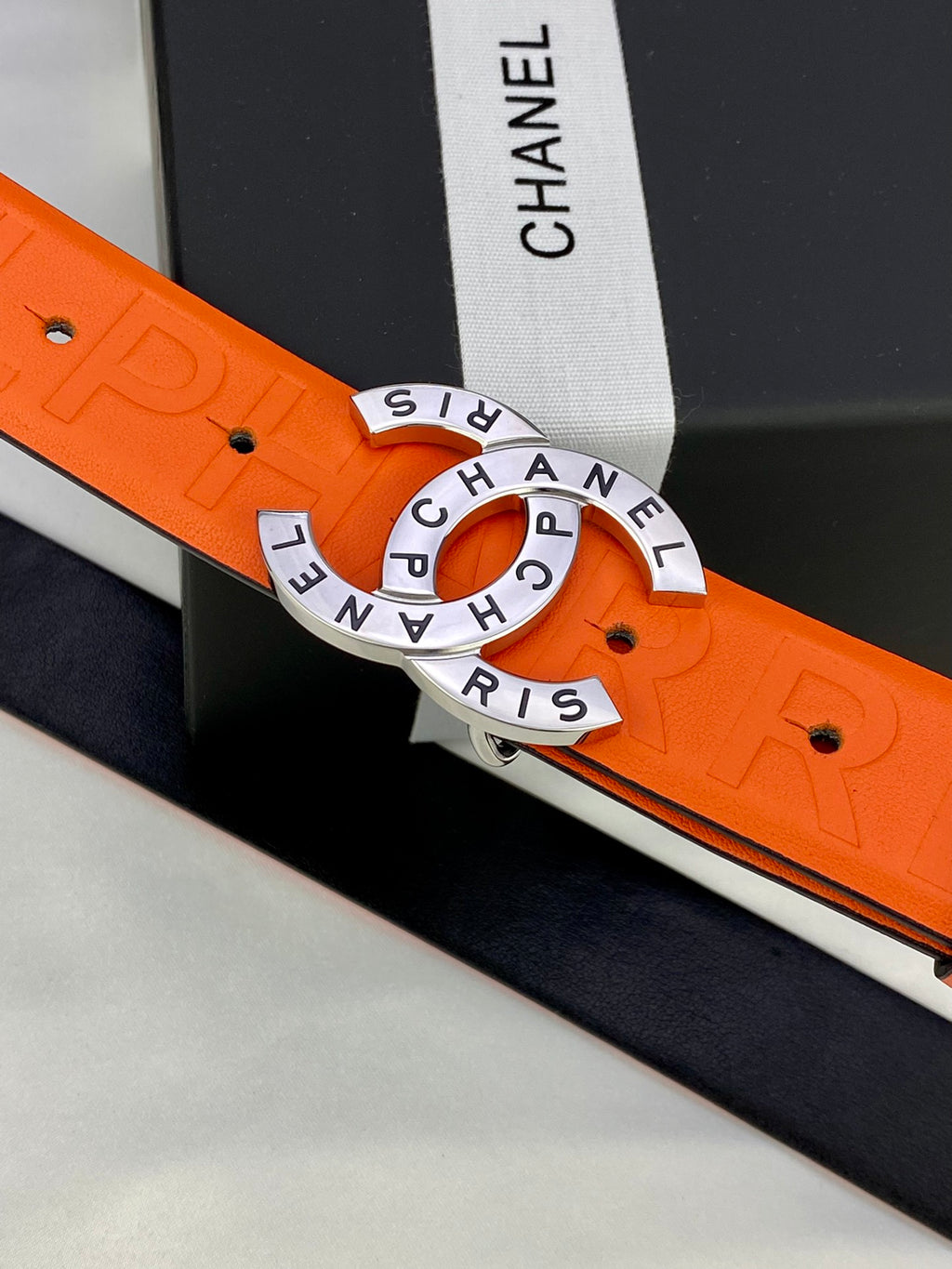 Chanel belt close-up: orange embossed strap and gold-tone circular logo buckle