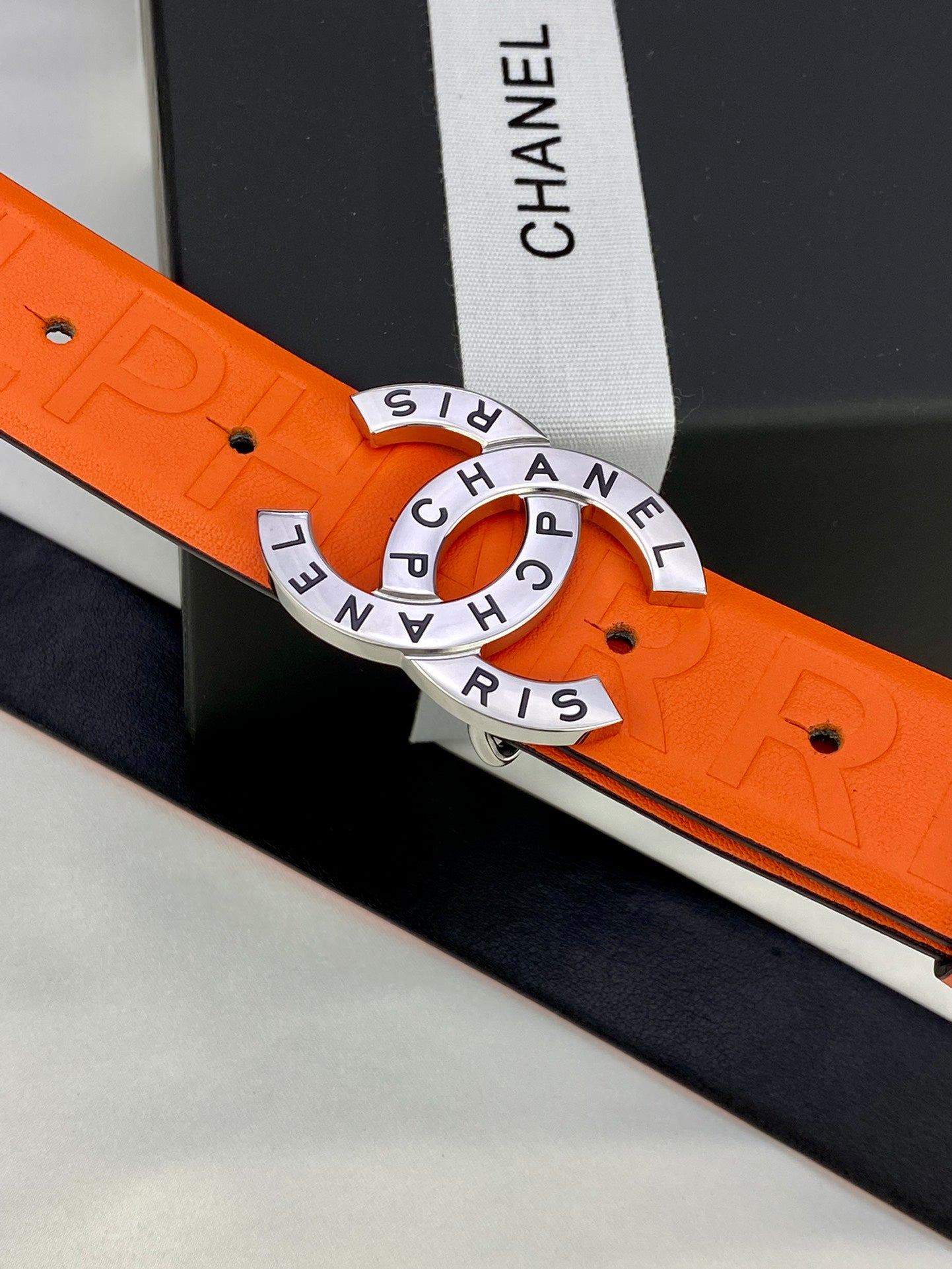 Chanel belt close-up: orange embossed strap and gold-tone circular logo buckle