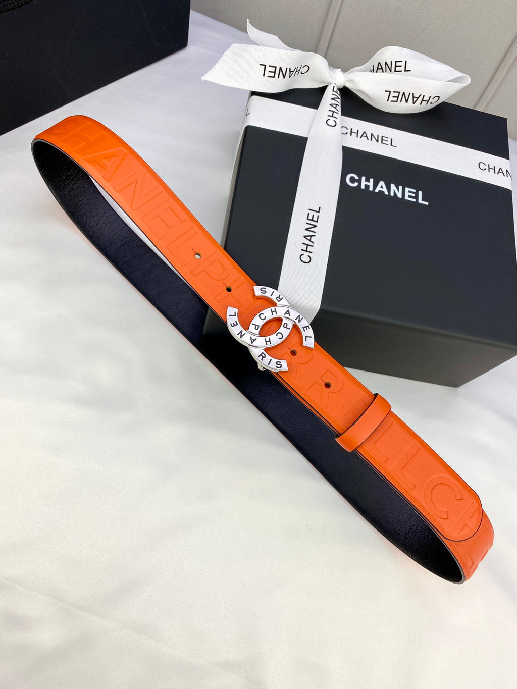 Chanel belt with orange strap and black underside, laid flat beside box