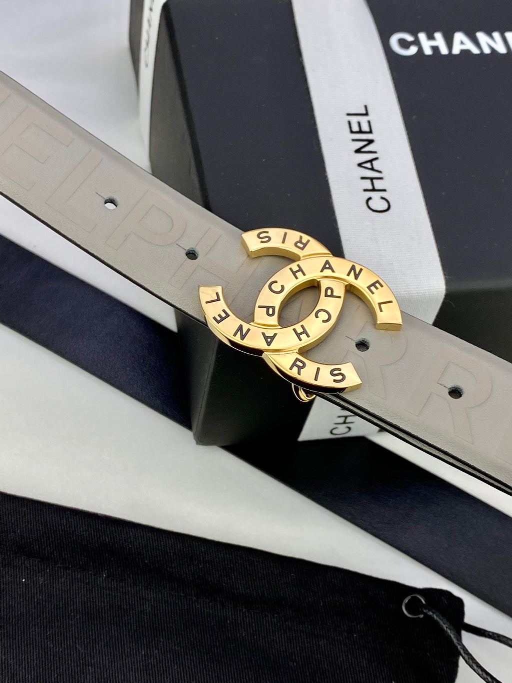 Beige Chanel belt buckle close-up with engraved circular logo on embossed strap