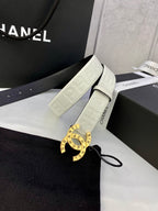 White Chanel belt with gold circular buckle, hanging from black bag