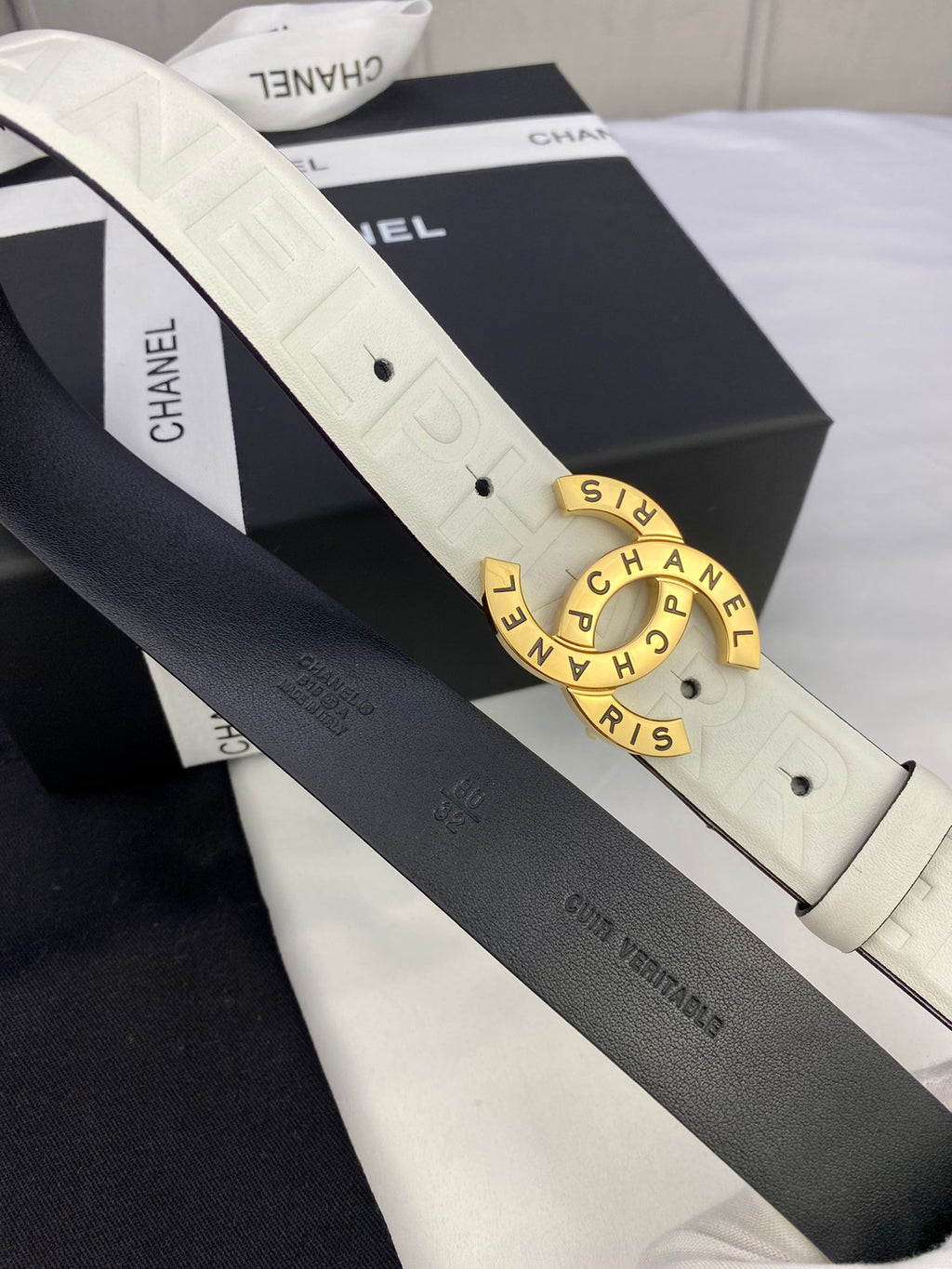White and dark Chanel belt straps with gold circular buckle and embossed lettering