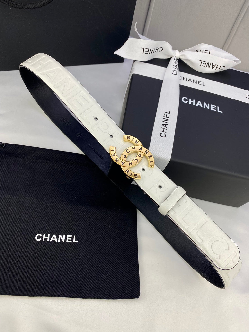 White Chanel belt with circular gold buckle and matching dark strap, flat lay