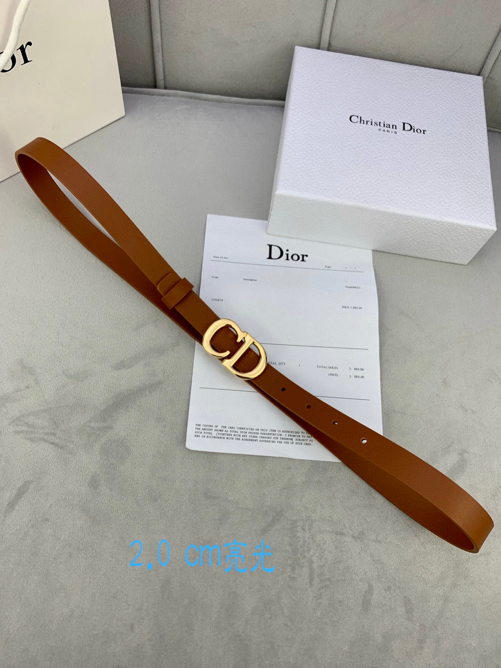 Tan leather belt with CD buckle next to Dior box and paperwork