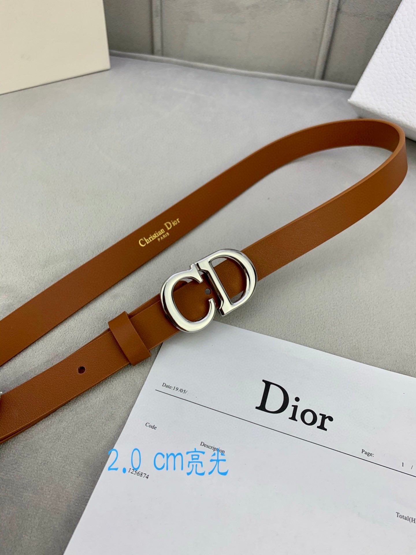 Tan leather belt with CD buckle on top of a Dior card
