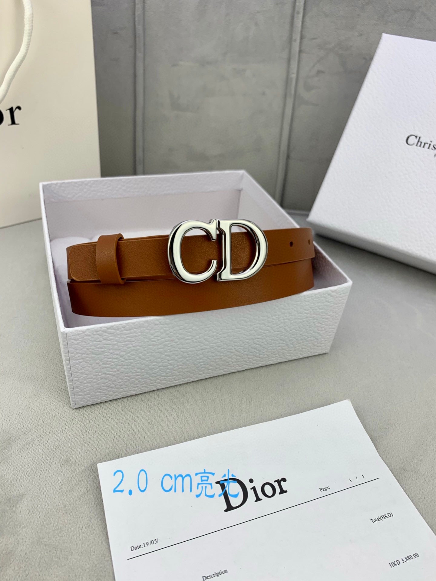 Tan leather belt with CD buckle inside a white gift box