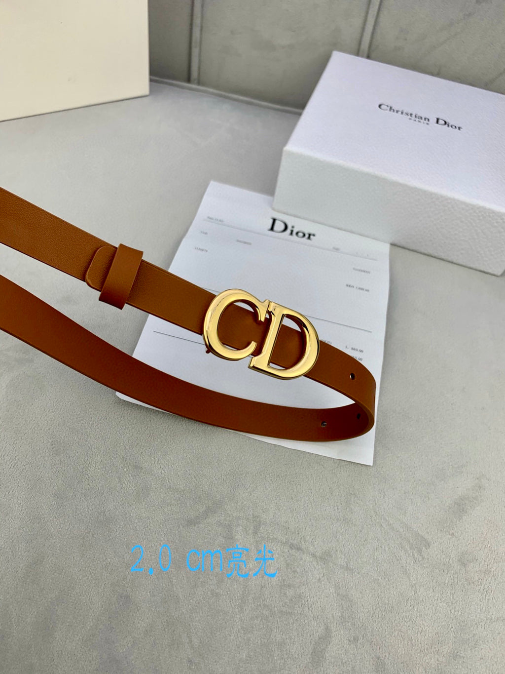 Tan leather belt with gold-tone CD buckle on a Dior card