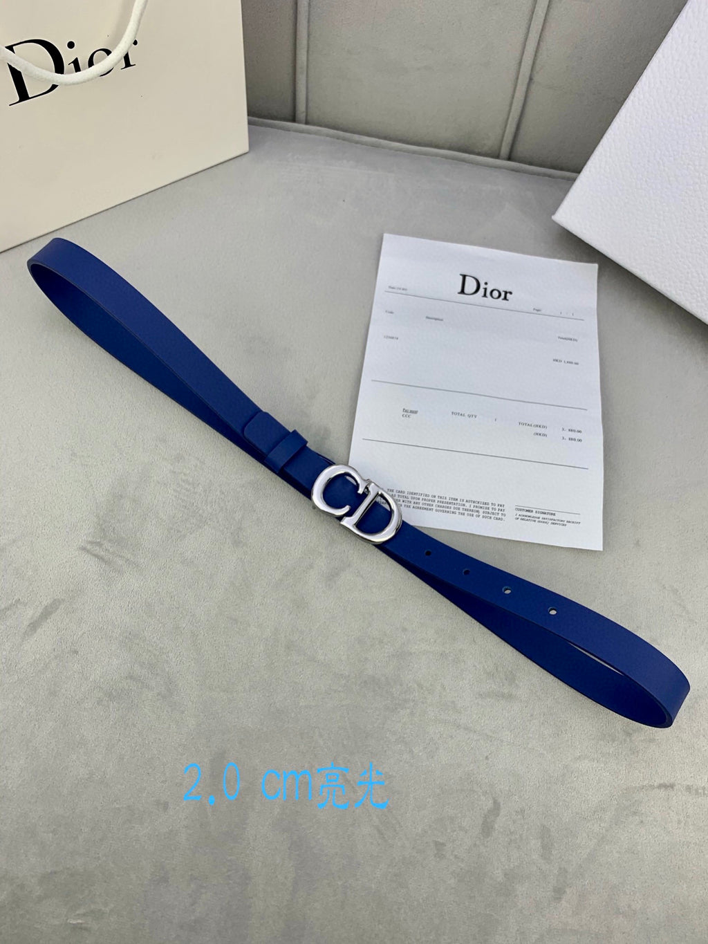 Blue Dior belt with CD logo buckle, shown diagonally with receipt card.