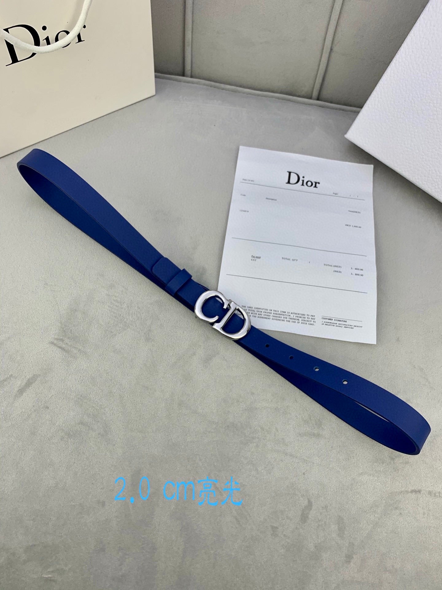 Blue Dior belt with CD logo buckle, shown diagonally with receipt card.