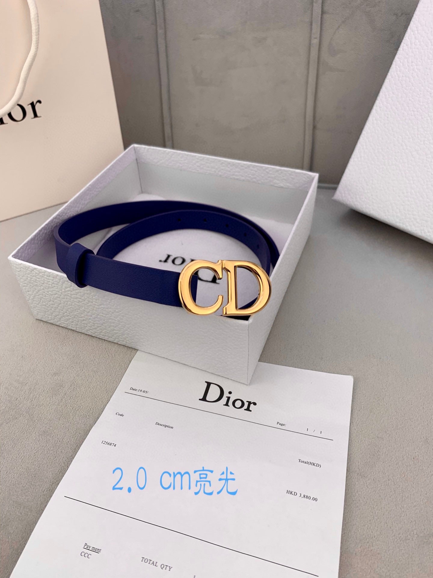 Blue Dior belt with CD logo buckle, resting in a branded box.