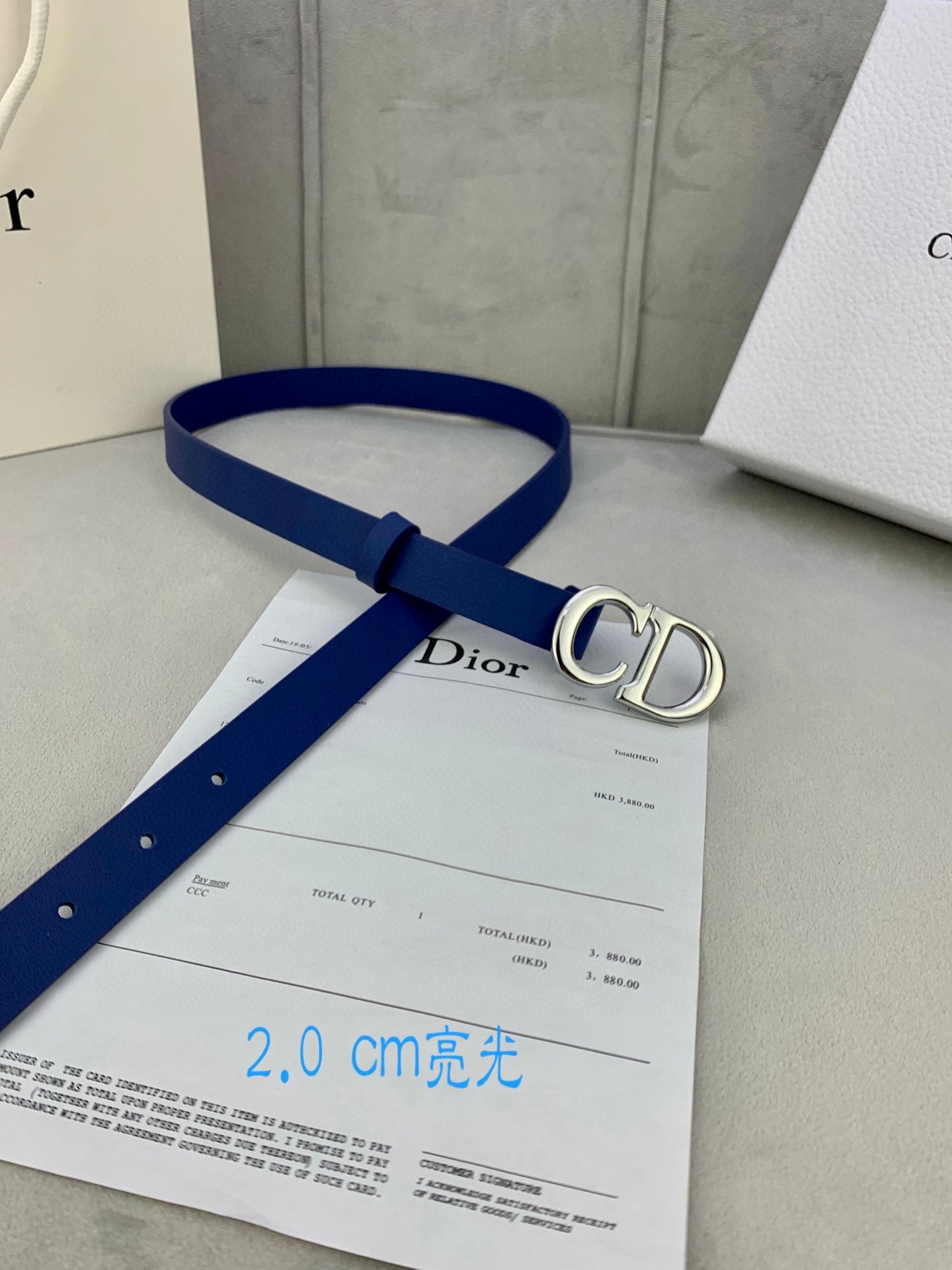 Blue Dior belt with CD logo buckle, displayed with paperwork and boxes.