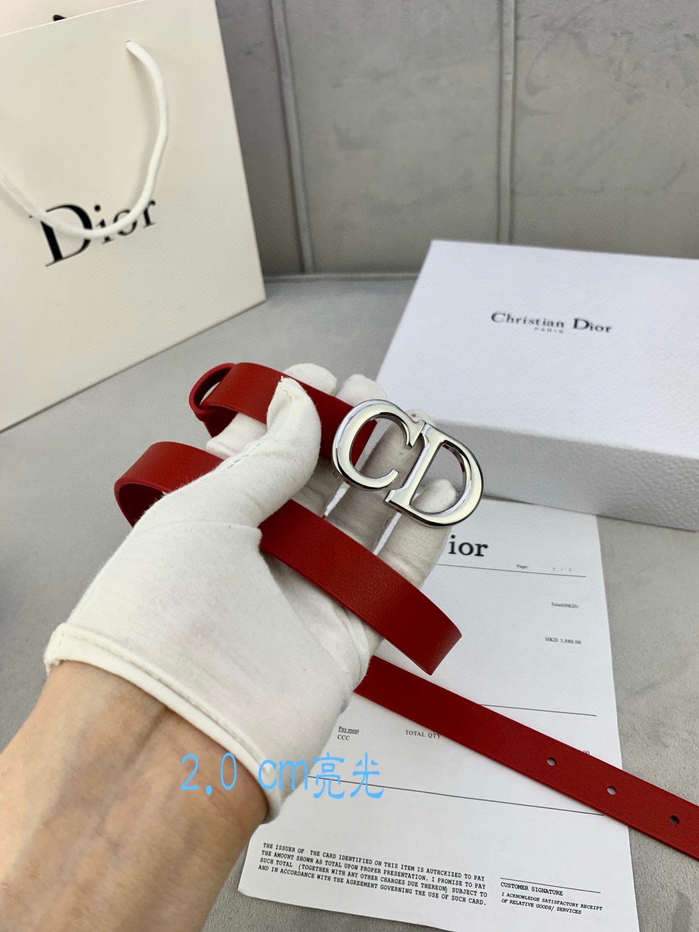 Dior red belt with CD buckle held in a white glove hand