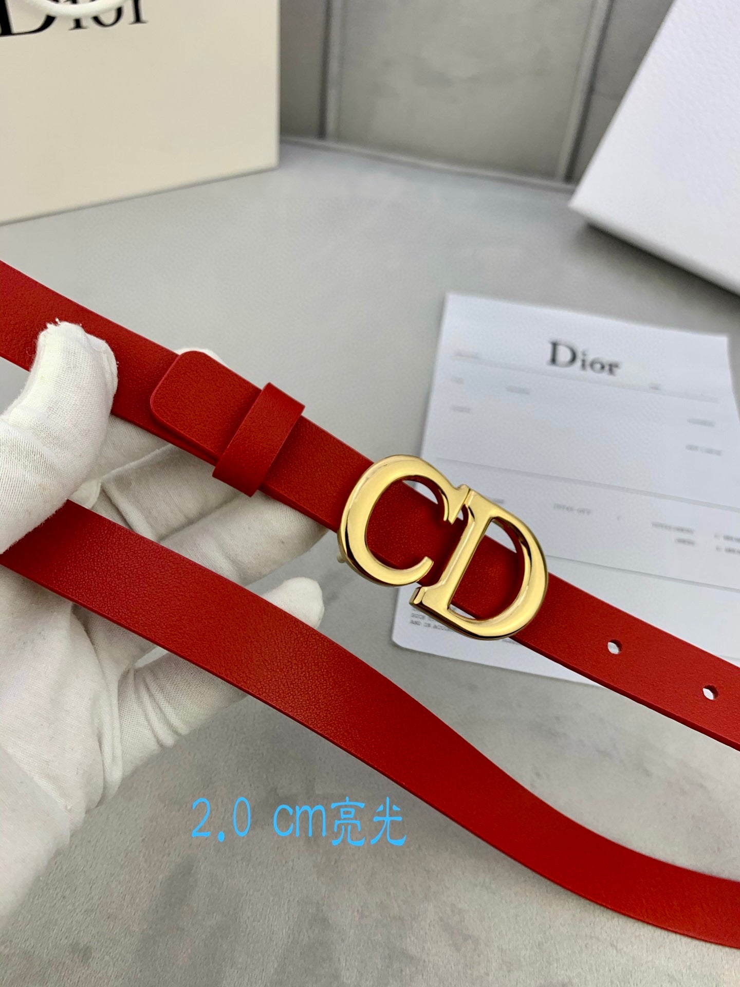 Dior red belt with CD buckle worn on a white glove hand