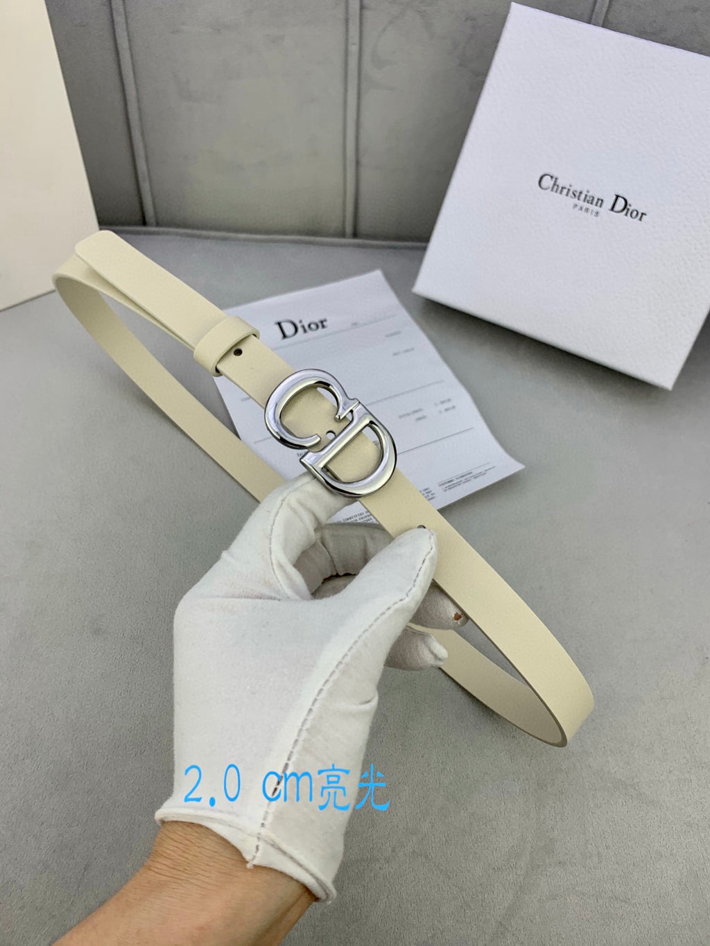 Beige belt with silver-tone CD buckle held in a hand