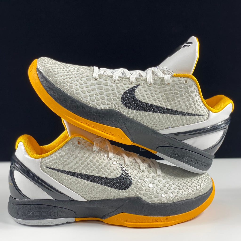 Nike basketball shoes with white textured uppers, yellow collars, black swooshes, gray soles