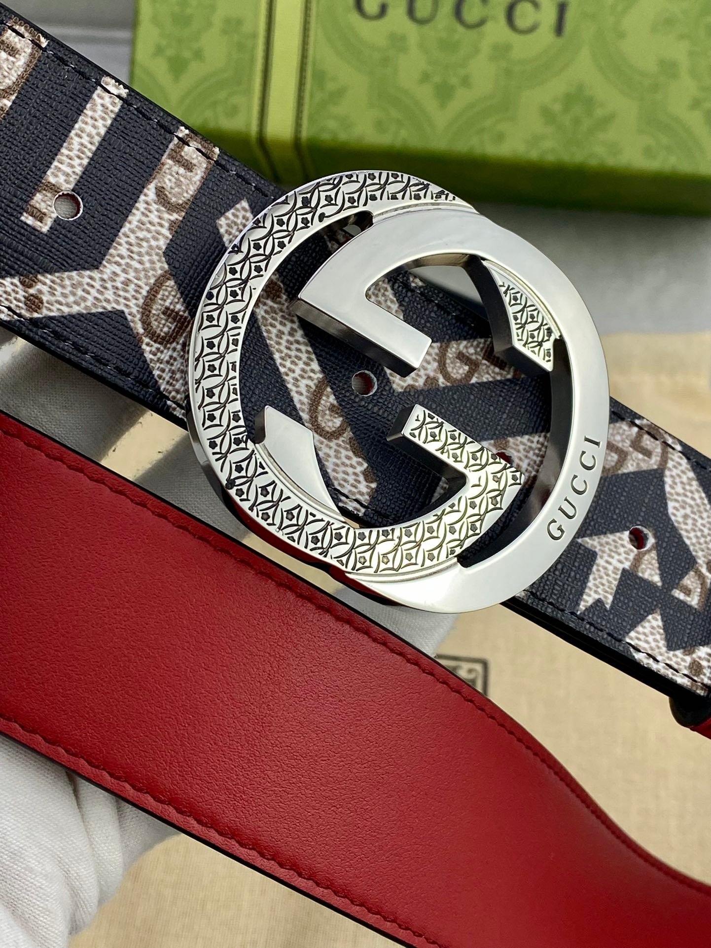 Gucci belt buckle close-up, circular engraved metal with navy GG canvas strap and red trim.