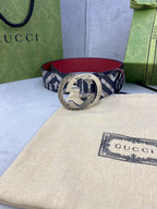 Gucci belt on dust bag, navy GG logo strap with red lining and gold circular buckle.