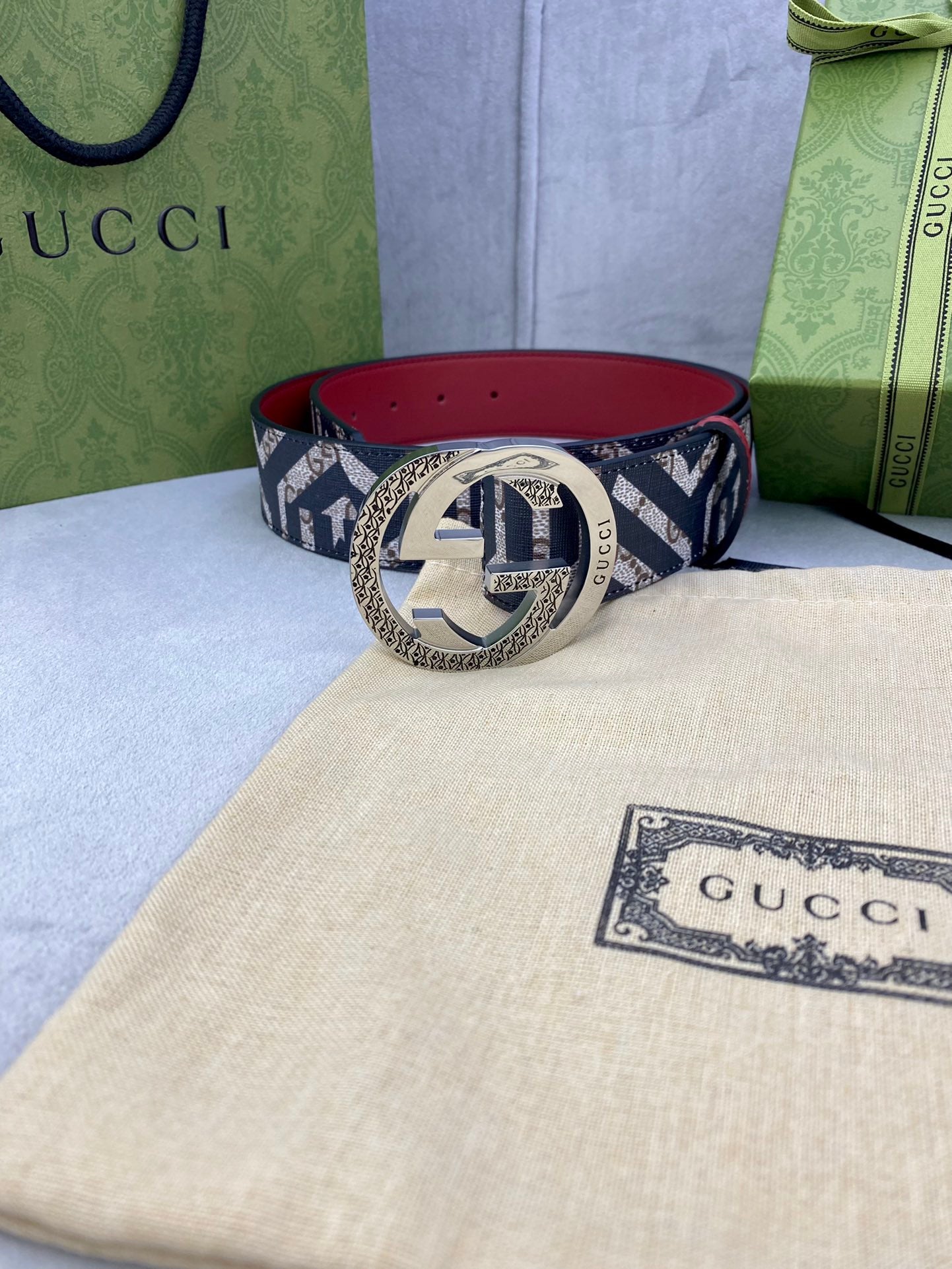 Gucci belt on dust bag, navy GG logo strap with red lining and gold circular buckle.