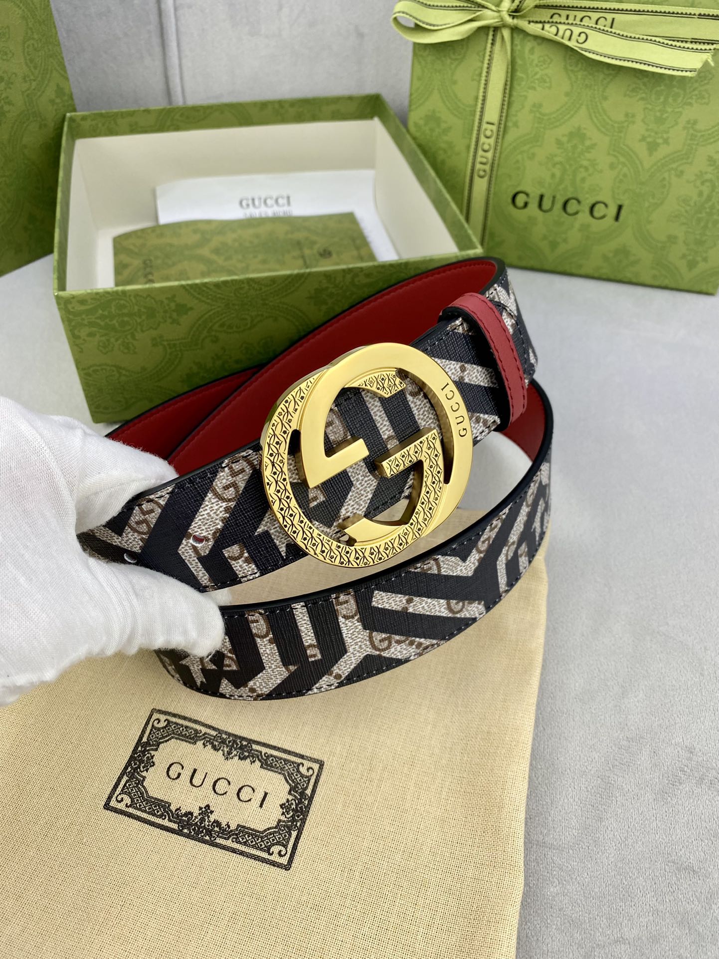 Gucci belt close-up on dust bag, navy GG canvas strap, red underside, gold interlocking buckle.