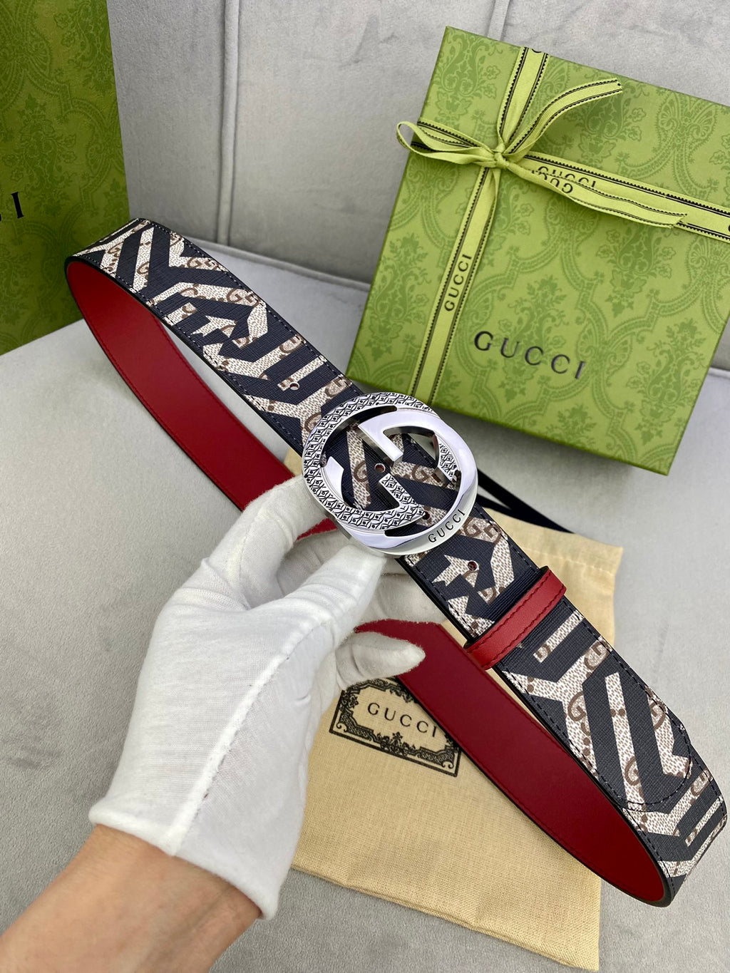 Gucci belt held in hand, navy GG canvas with red leather underside and silver-toned buckle.