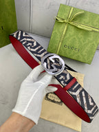 Gucci belt held in hand, navy GG canvas with red leather underside and silver-toned buckle.