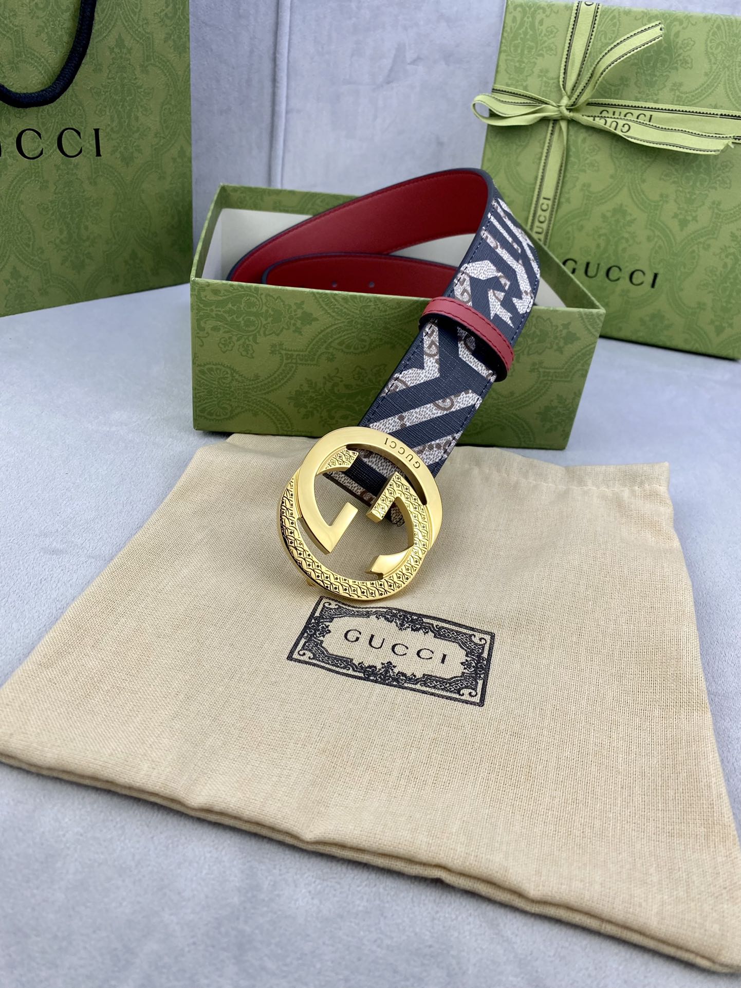 Gucci belt on box and dust bag, navy GG logo strap with red edge and gold buckle.