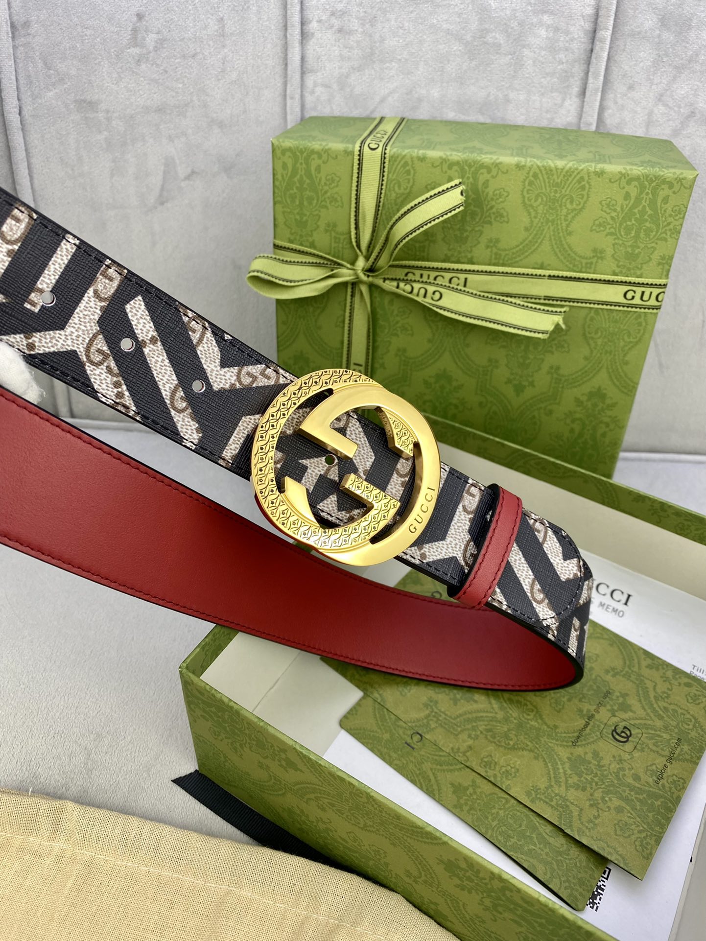 Gucci belt laid flat, navy GG pattern strap with red leather underside and gold buckle.