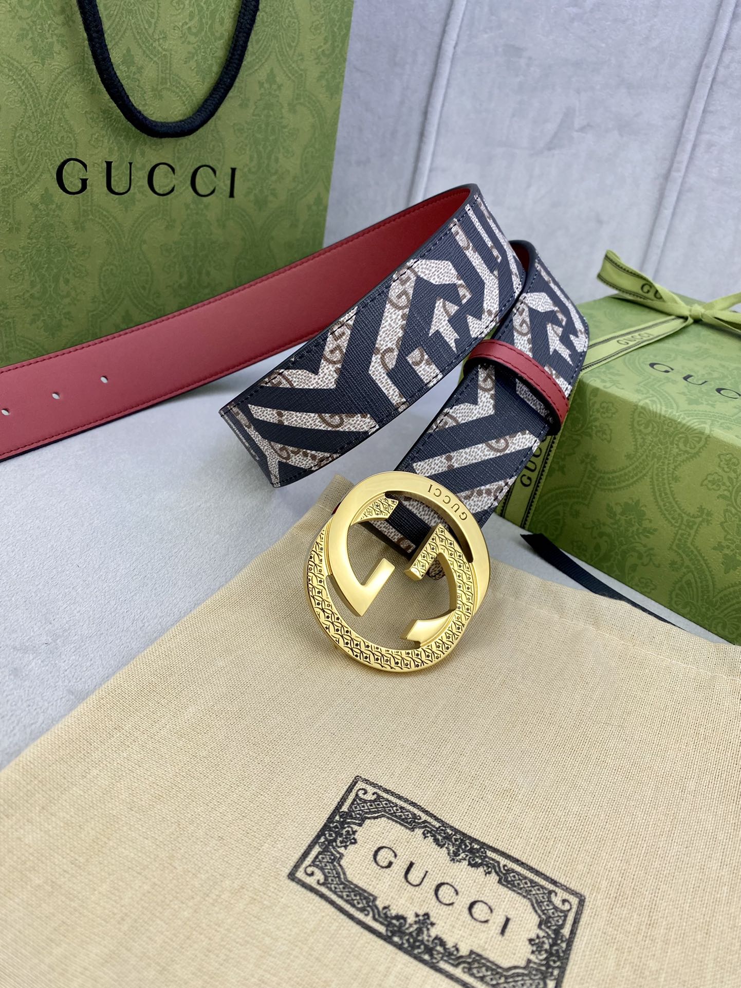 Gucci belt with navy GG logo strap, red leather strap back, gold round buckle and ring detail.