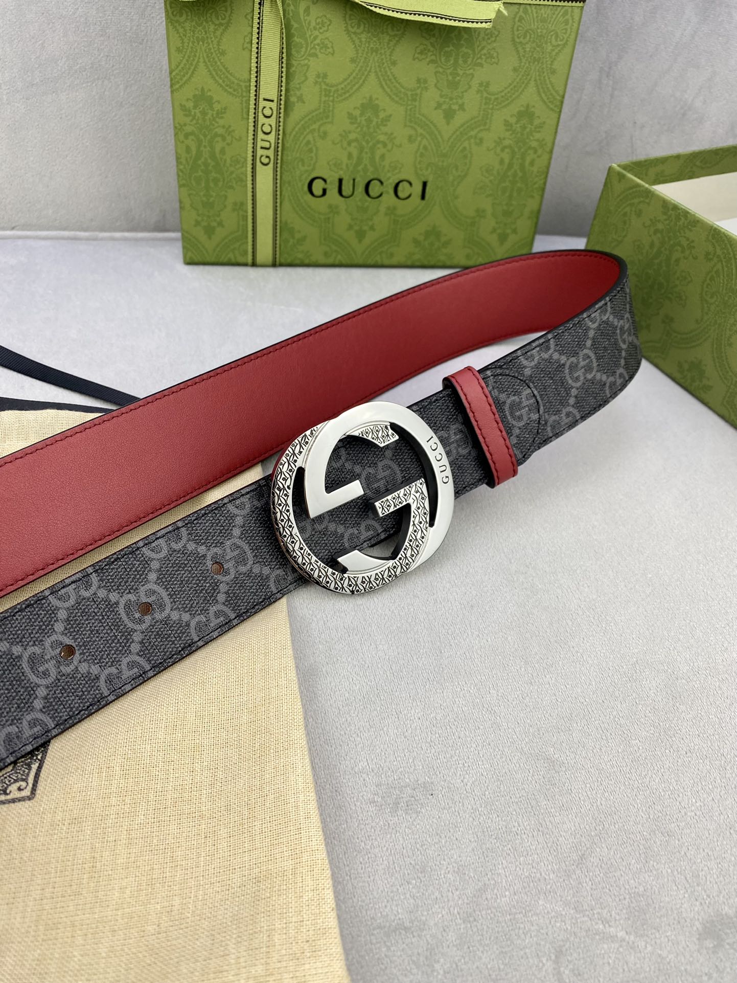 Gucci belt buckle close-up: silver-toned GG on dark monogram strap, red edge.